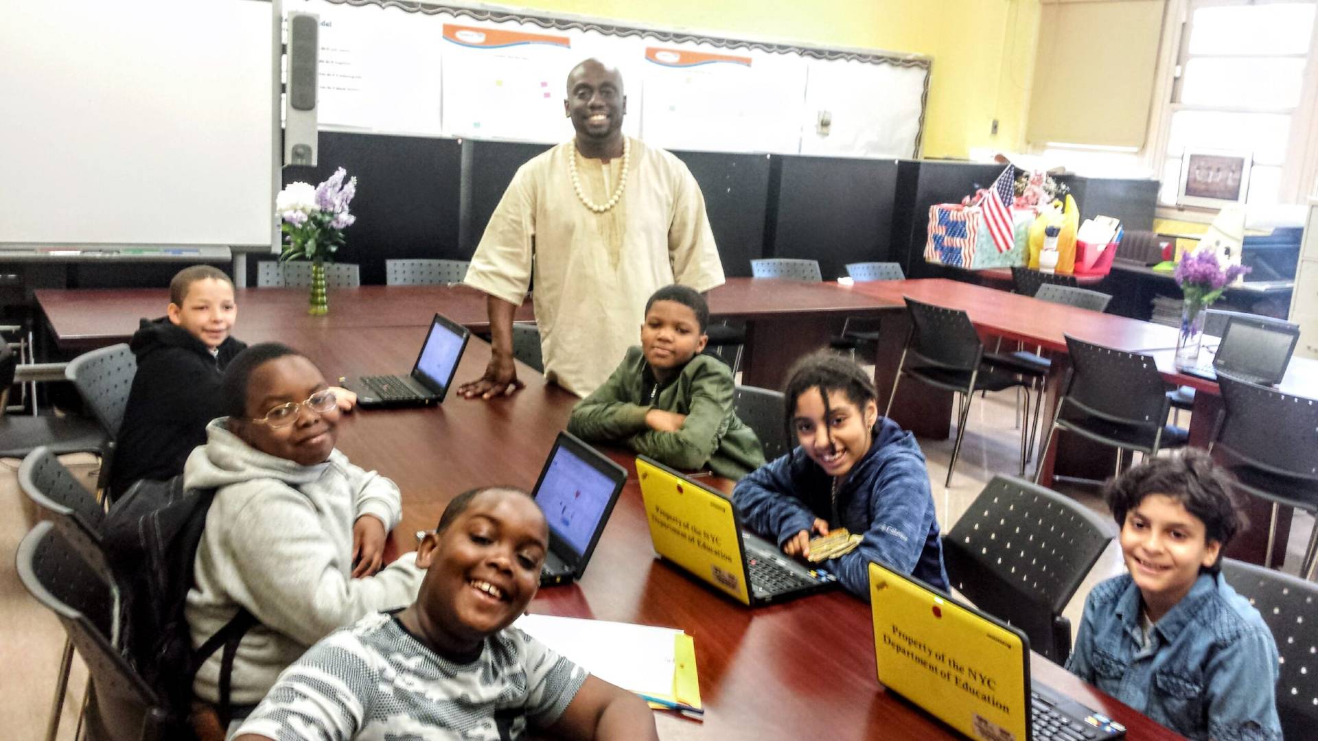 A group of Saturday program students with computers on a table, take a photo during graphic design class with their instructor.